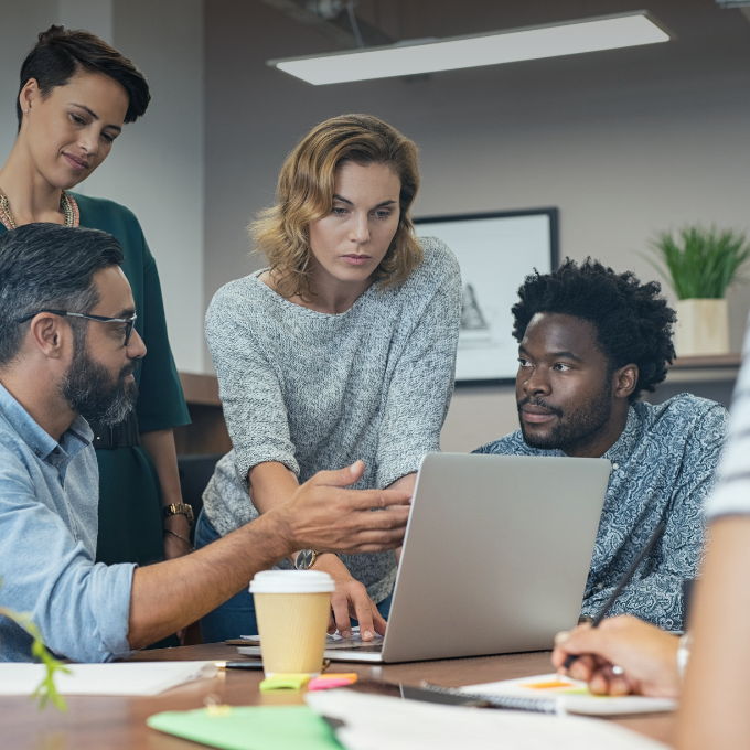 Group of colleagues stood and sat around a desk looking at a laptop.